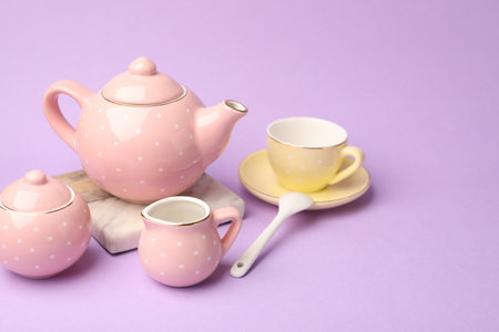 Beautiful ceramic tea set for children on violet background, closeup. Space for textの写真素材