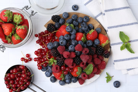 Different ripe berries and mint leaves on white tiled table, flat lay