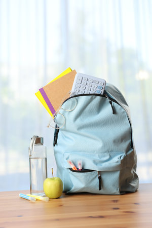 Backpack, different stationery, bottle of water and apple on desk in classroom
