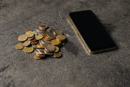 Smartphone and coins on gray table, closeup