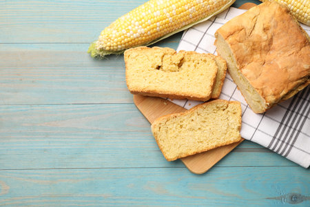 Freshly baked cornbread and cobs on light blue wooden table, flat lay. Space for text