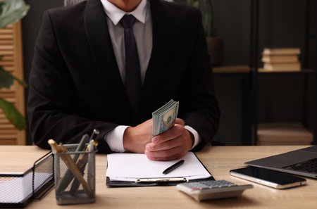 Man counting dollar banknotes at wooden table, closeup