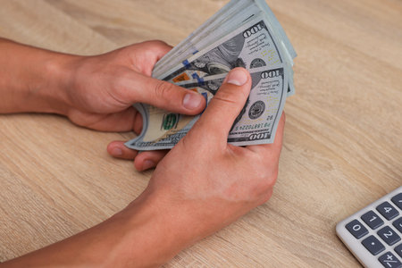 Man counting dollar banknotes at wooden table, closeup