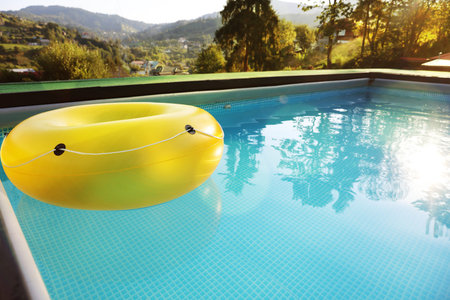 Yellow inflatable ring in swimming pool outdoors, space for text