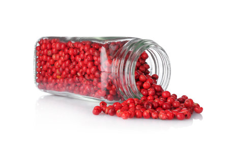 Red peppercorns in glass jar isolated on white. Aromatic spice