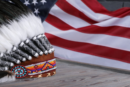 Native American chief headdress (feathered war bonnet) on wooden surface against American flag, closeup. Space for textの写真素材