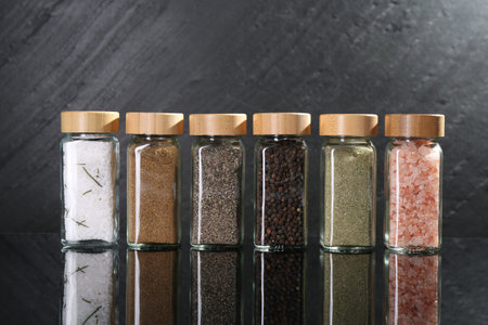 Different spices in glass jars on mirror surface