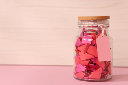 Color paper pieces in glass jar on pink table, space for textの写真素材