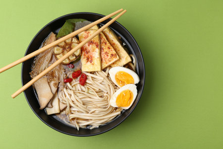 Tasty ramen with enoki and oyster (eryngii) mushrooms in bowl on green table, top view