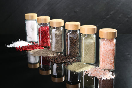Different spices and glass jars on mirror surfaceの写真素材