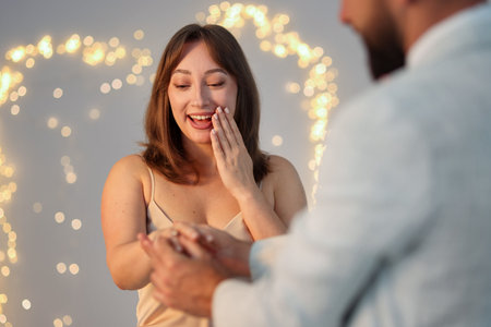 Making marriage proposal. Man putting engagement ring on his girlfriend's finger against light gray background, closeup. Bokeh effectの写真素材