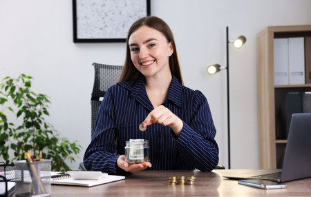 Woman putting coin into glass jar at wooden table indoors