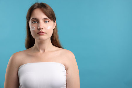 Beautiful woman with cream on her face against light blue background. Space for textの写真素材
