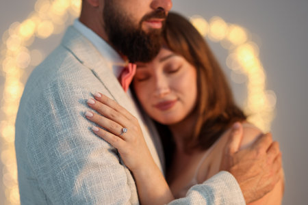 Making marriage proposal. Woman with engagement ring and her fiance hugging on light gray background, bokeh effectの写真素材