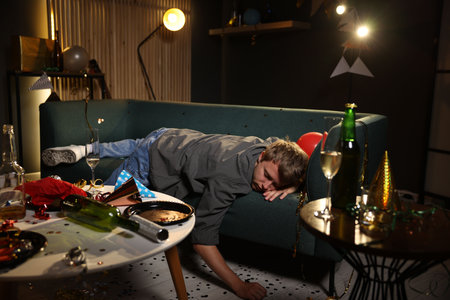 Man suffering from hangover on sofa in messy room after party