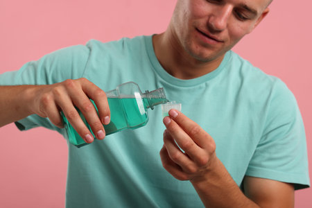 Man pouring mouthwash into cap on pink background, closeup