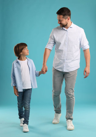 Father and son holding hands while walking on light blue backgroundの写真素材