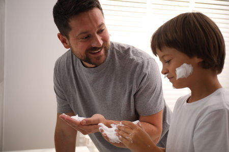 Father and son applying shaving foam on their faces in bathroom