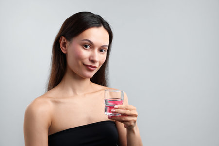 Young woman with cap of mouthwash on gray background, space for text. Oral hygiene
