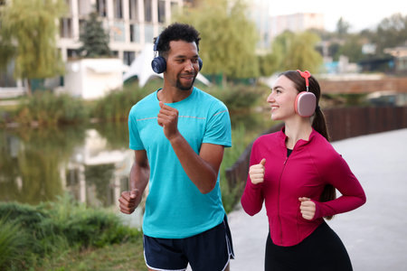 Smiling couple in headphones running near river outdoors