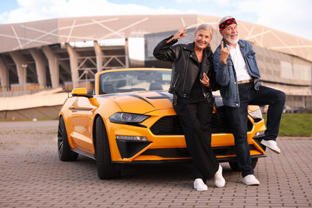 Stylish senior couple near modern cabriolet showing rock gesture outdoorsの写真素材