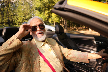Stylish senior man in sunglasses driving modern cabriolet outdoorsの写真素材