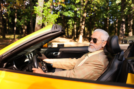 Stylish senior man in sunglasses driving modern cabriolet outdoorsの写真素材
