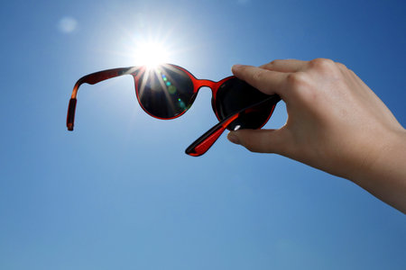 Woman holding stylish sunglasses against blue sky on sunny day, low angle view