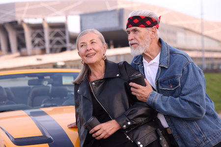 Stylish senior couple with takeaway coffee near modern cabriolet outdoors