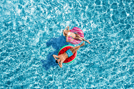 Happy couple with inflatable rings in swimming pool, top view. Summer vacation