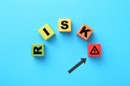 Word Risk of wooden cubes with letters on light blue background, top view. Arrow pointing at warning...