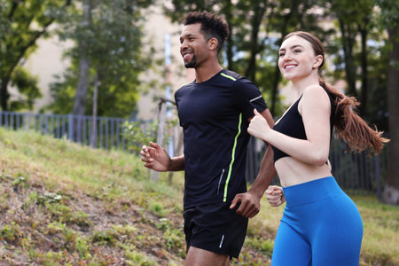 Smiling couple in sportswear running in park, low angle view. Space for text