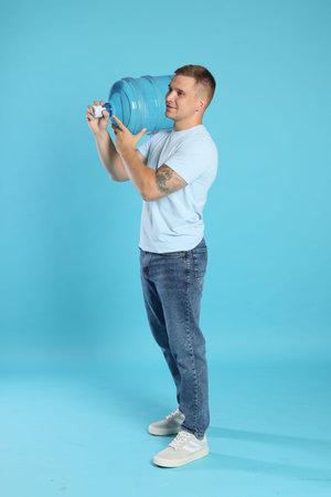 Delivery man with cooler bottle of water on light blue background