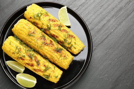 Tasty grilled corncobs with dill and lime slices on black table, flat lay
