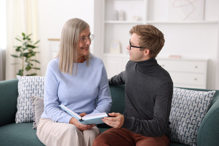 Smiling mother and her son in glasses reading book on sofa at home