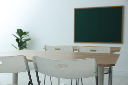 Blank green chalkboard, desks, chairs and plant in classroom, closeupの写真素材