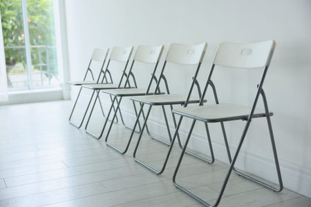 Many stylish chairs near white wall in room