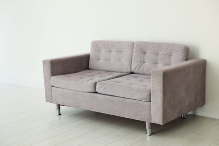 Comfortable gray sofa near white wall in room