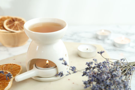 Aroma lamp with burning candle, lavender and dry orange slices on white table, closeup
