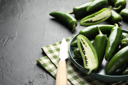 Fresh jalapeno peppers and knife on black textured table, closeup.