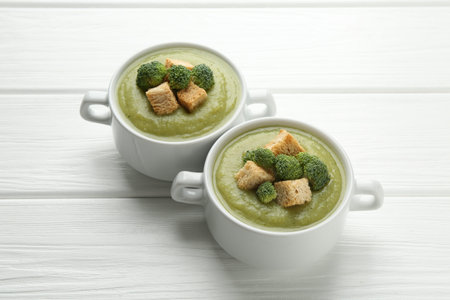 Tasty broccoli cream soup with croutons in bowls on white wooden table, closeup