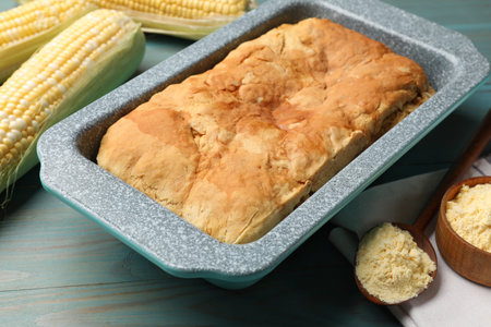 Freshly baked cornbread, flour and cobs on light blue wooden table, closeup