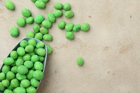 Wasabi coated peanuts and scoop on gray textured table, flat lay. Space for text