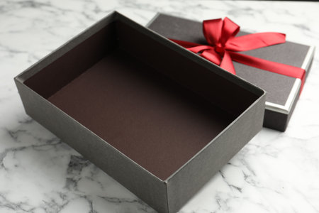 Opened gift box with beautiful lid on white marble table, closeup