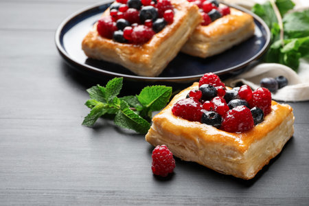Tasty puff pastries with berries and mint on gray wooden table, closeup. Space for textの写真素材