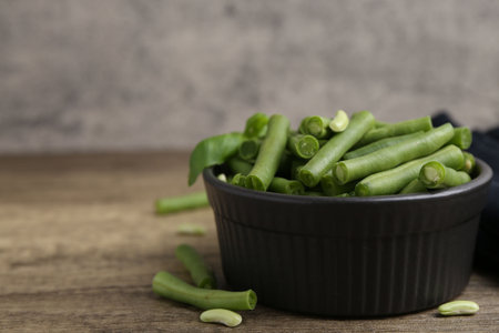 Pieces of fresh green beans in bowl on wooden table, closeup. Space for text