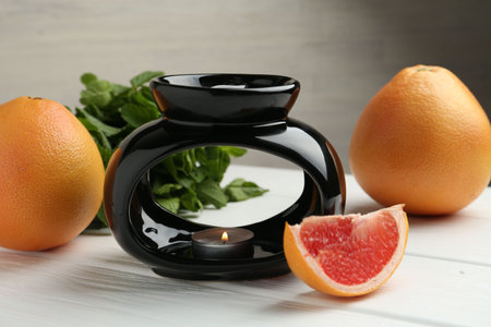 Aroma lamp with burning candle, mint leaves and grapefruits on white wooden table against gray...