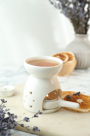 Aroma lamp with burning candle, lavender and dry orange slices on white table, closeup