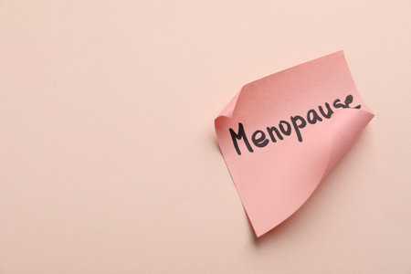Paper note with the word Menopause on beige background, closeup. Space for text