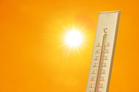 Thermometer showing high temperature against orange sky with bright sun. Extremely hot weather